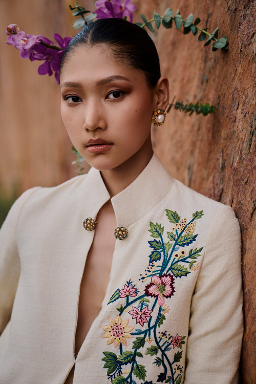 Woman wearing a cream-colored blazer with floral embroidery against a wooden background